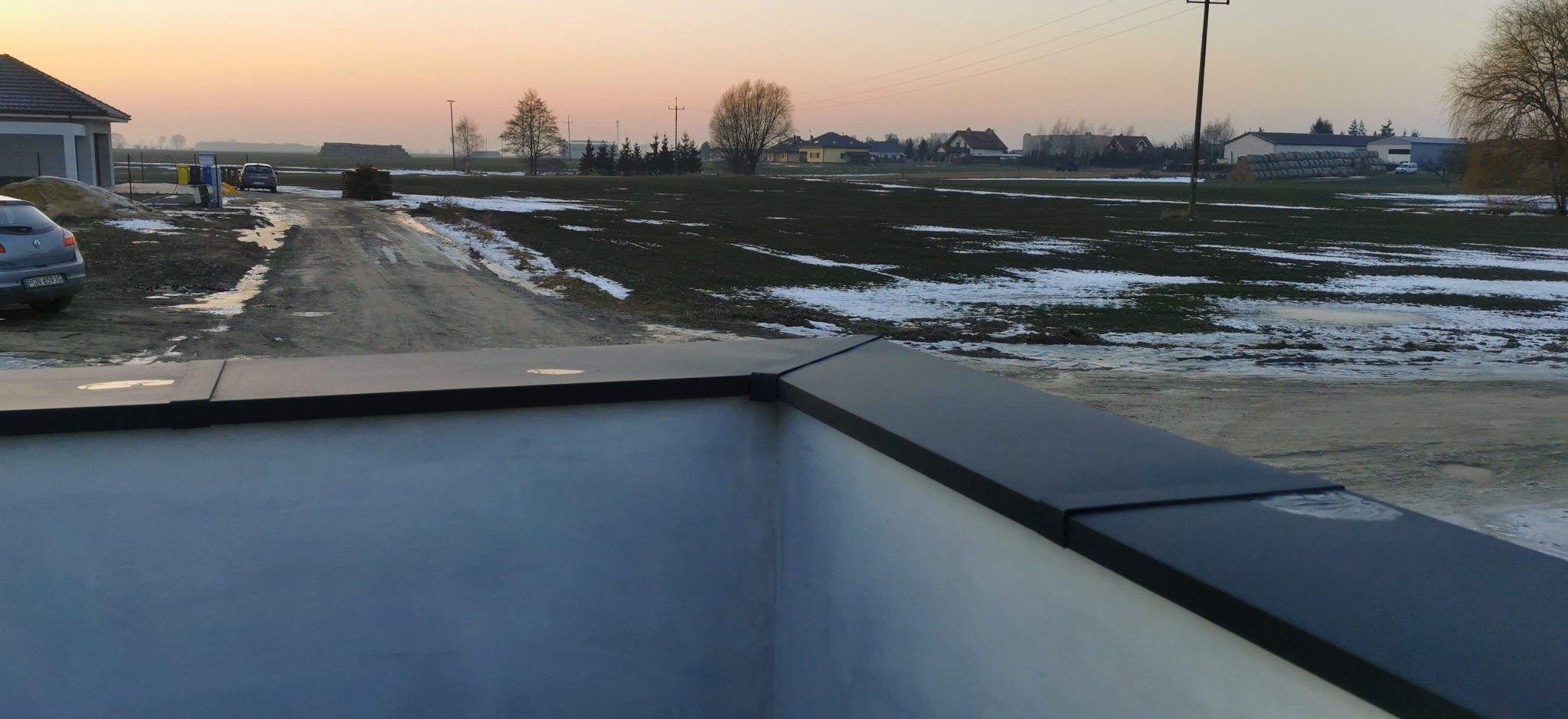 Nowoczesne obróbki blacharskie na dachu budynku, widok z góry na tle zimowego krajobrazu o zmierzchu. Detal wykończenia dachu.