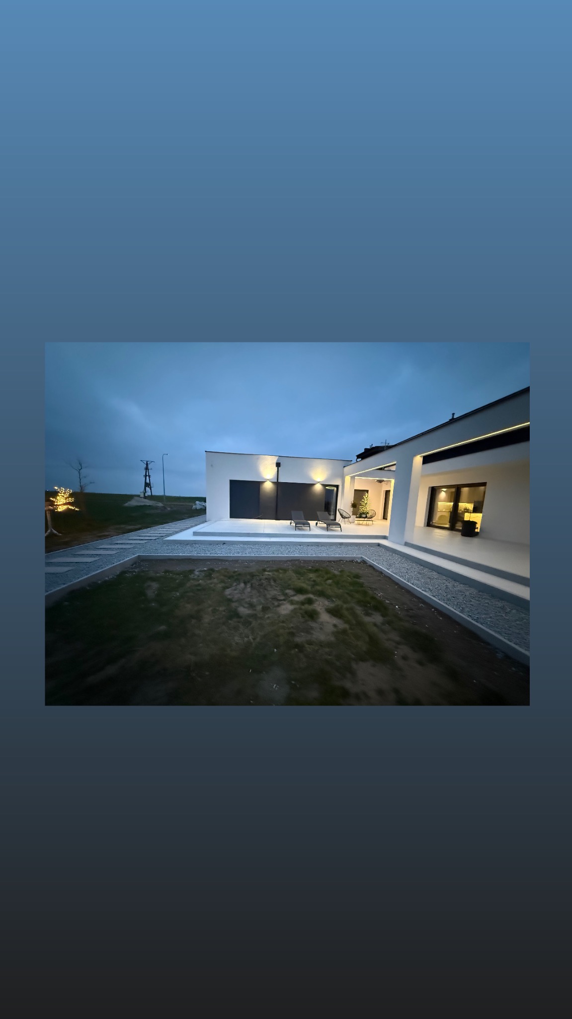 Nowoczesny dom jednorodzinny z płaskim dachem i oświetleniem zewnętrznym, widok z ogrodu o zmierzchu. Minimalistyczna architektura, jasna elewacja, ciemne akcenty.