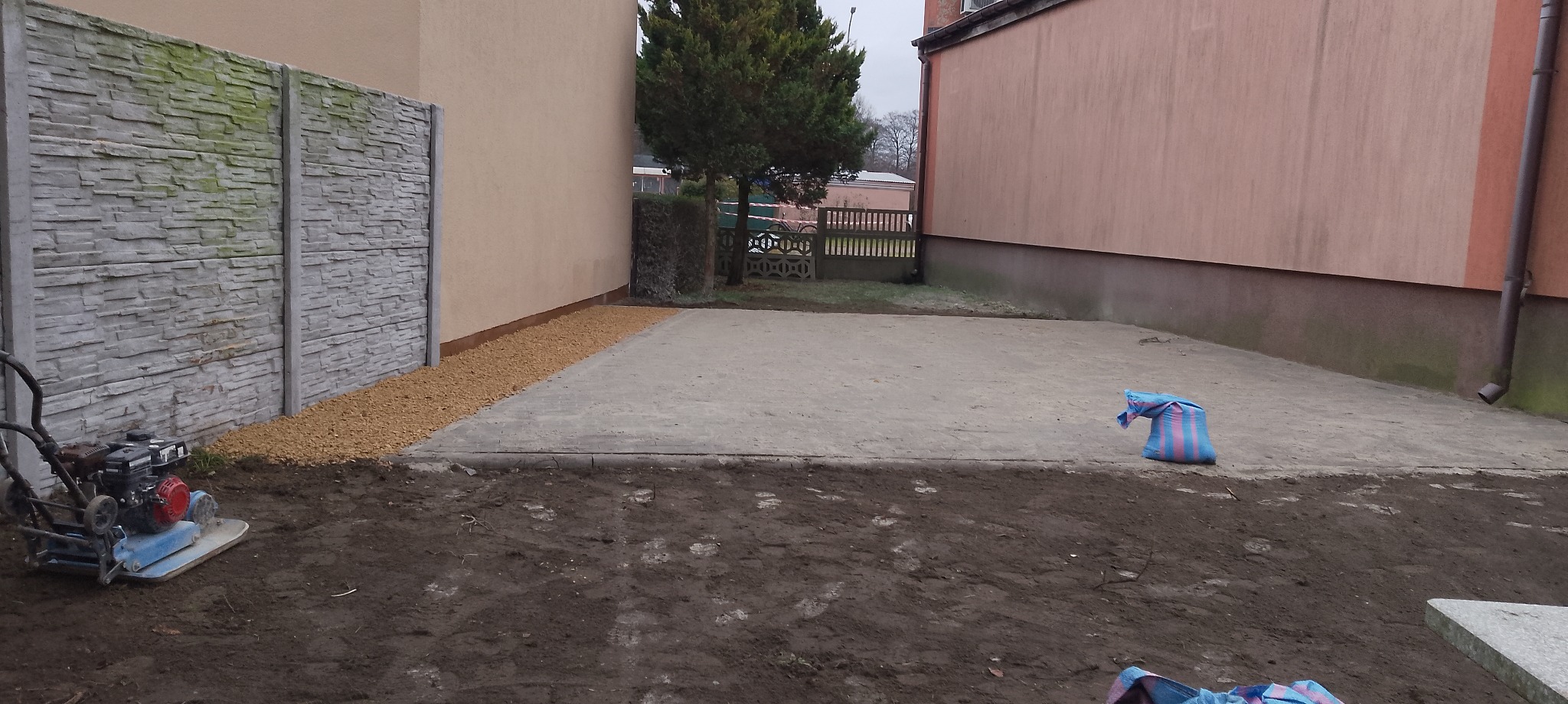 Przygotowanie podłoża pod nawierzchnię: ubijarka spalinowa, podsypka z kruszywa, betonowa płyta, ogrodzenie z paneli imitujących kamień. Prace ziemne.