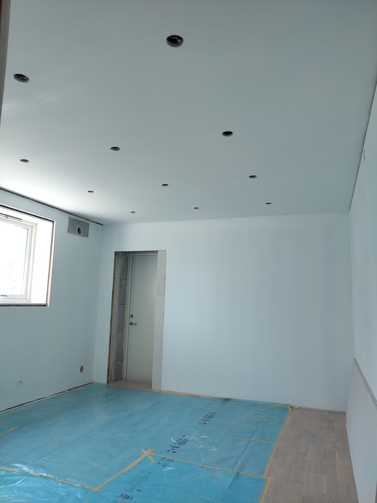 Wnętrze po wygłuszeniu ścian płytami farmacel, przygotowane do malowania. Widoczne profile, otwory na oświetlenie w suficie i zabezpieczona podłoga.