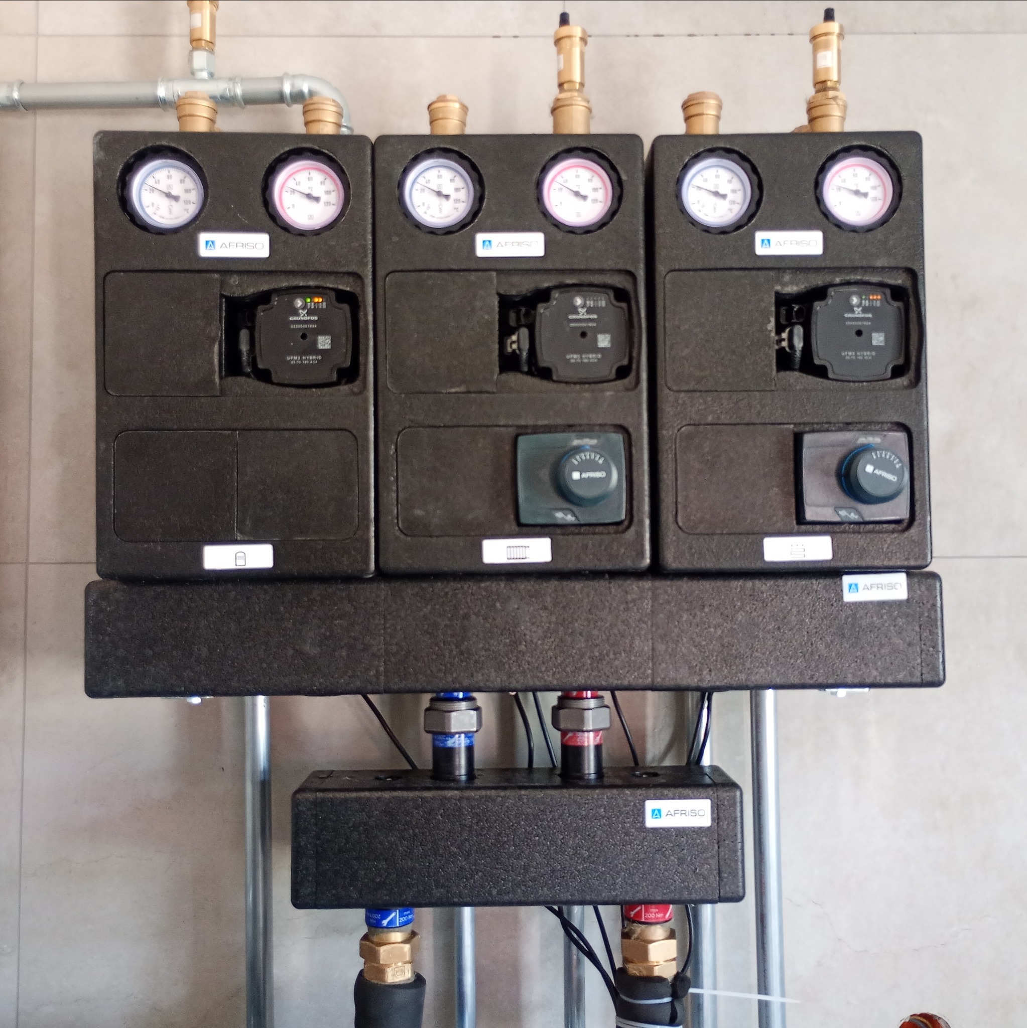 Rozdzielacz ogrzewania podłogowego Afriso z manometrami i pompami obiegowymi, zamontowany w kotłowni w Goniądz. Instalacja grzewcza z rurami.
