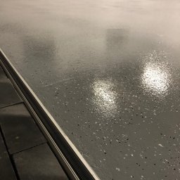 Piotr Biegun - Błyszcząca, szara posadzka z drobnymi, ciemnymi wtrąceniami, wykończona listwą przypodłogową. Widoczne refleksy światła podkreślają gładką powierzchnię.