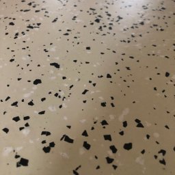 Piotr Biegun - Beżowa posadzka z czarnymi i białymi elementami dekoracyjnymi, tworzącymi wzór lastryko. Gładka powierzchnia, widoczne drobne detale i faktura materiału.