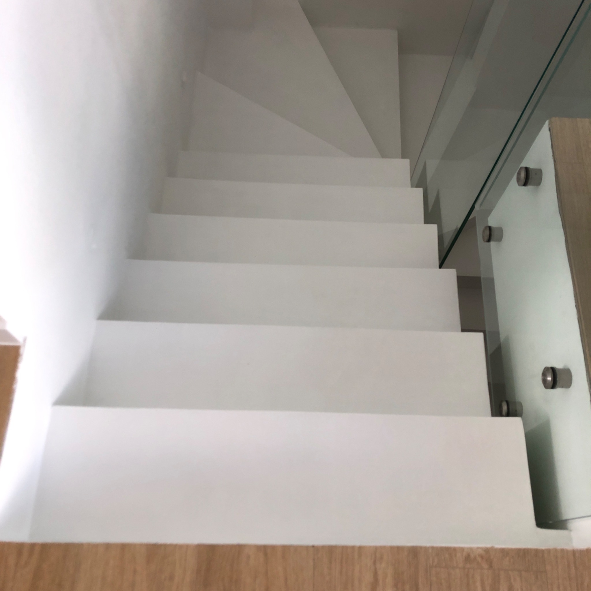 Białe schody z mikrocementu z szklaną balustradą, widok z góry. Minimalistyczny design, gładka powierzchnia, nowoczesne wykończenie.