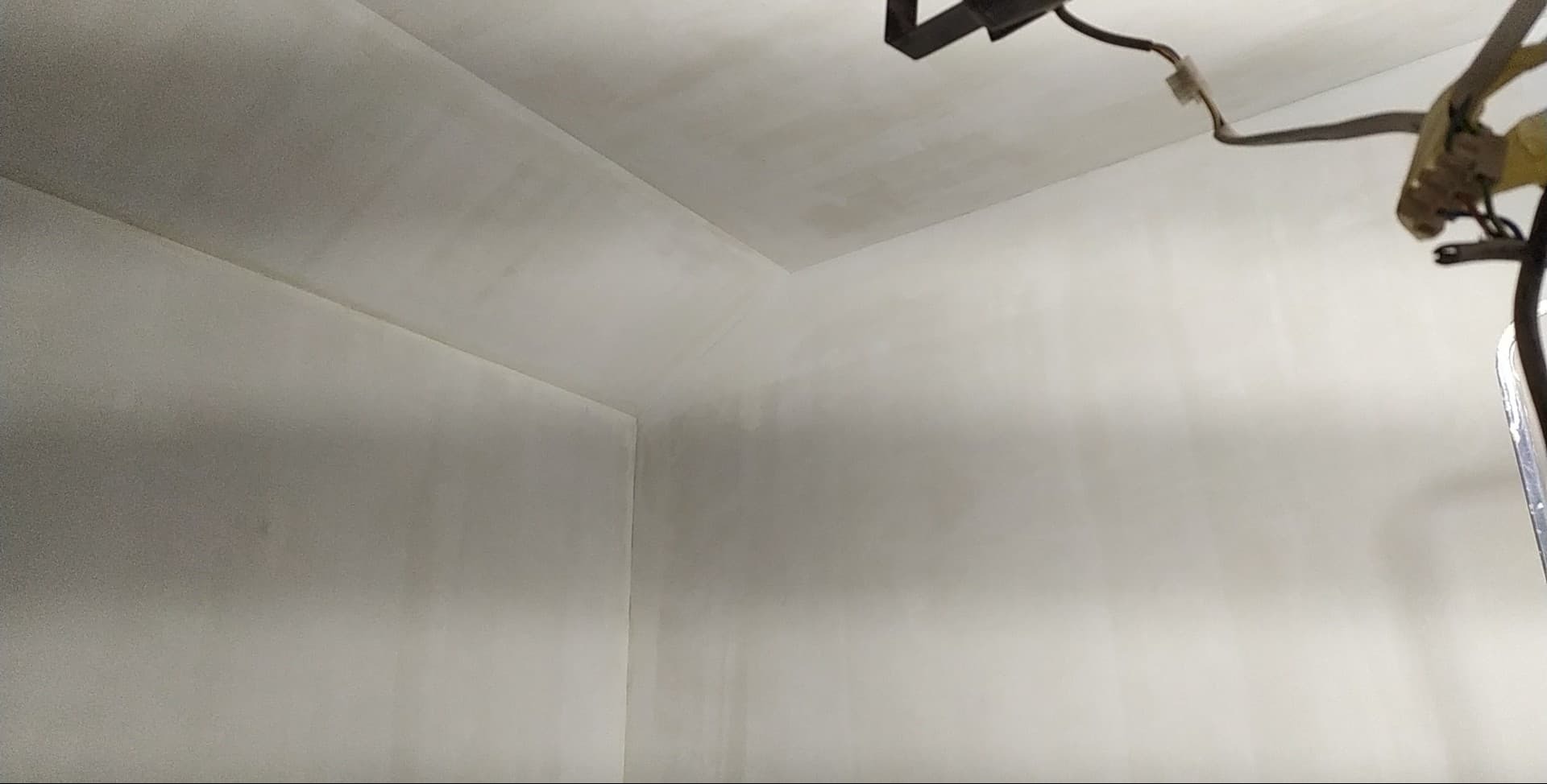 Wnętrze po szpachlowaniu: gładkie, białe ściany i sufit w rogu pomieszczenia, widoczne ślady po pracy, drabina w prawym górnym rogu kadru.