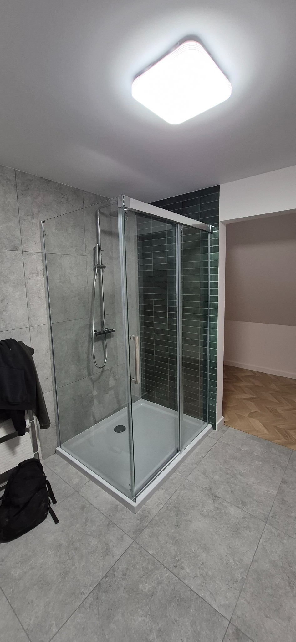 Nowoczesna kabina prysznicowa z szarymi płytkami w tle i zielonym akcentem, widok z boku. Realizacja w Lublinie. Minimalistyczny design.