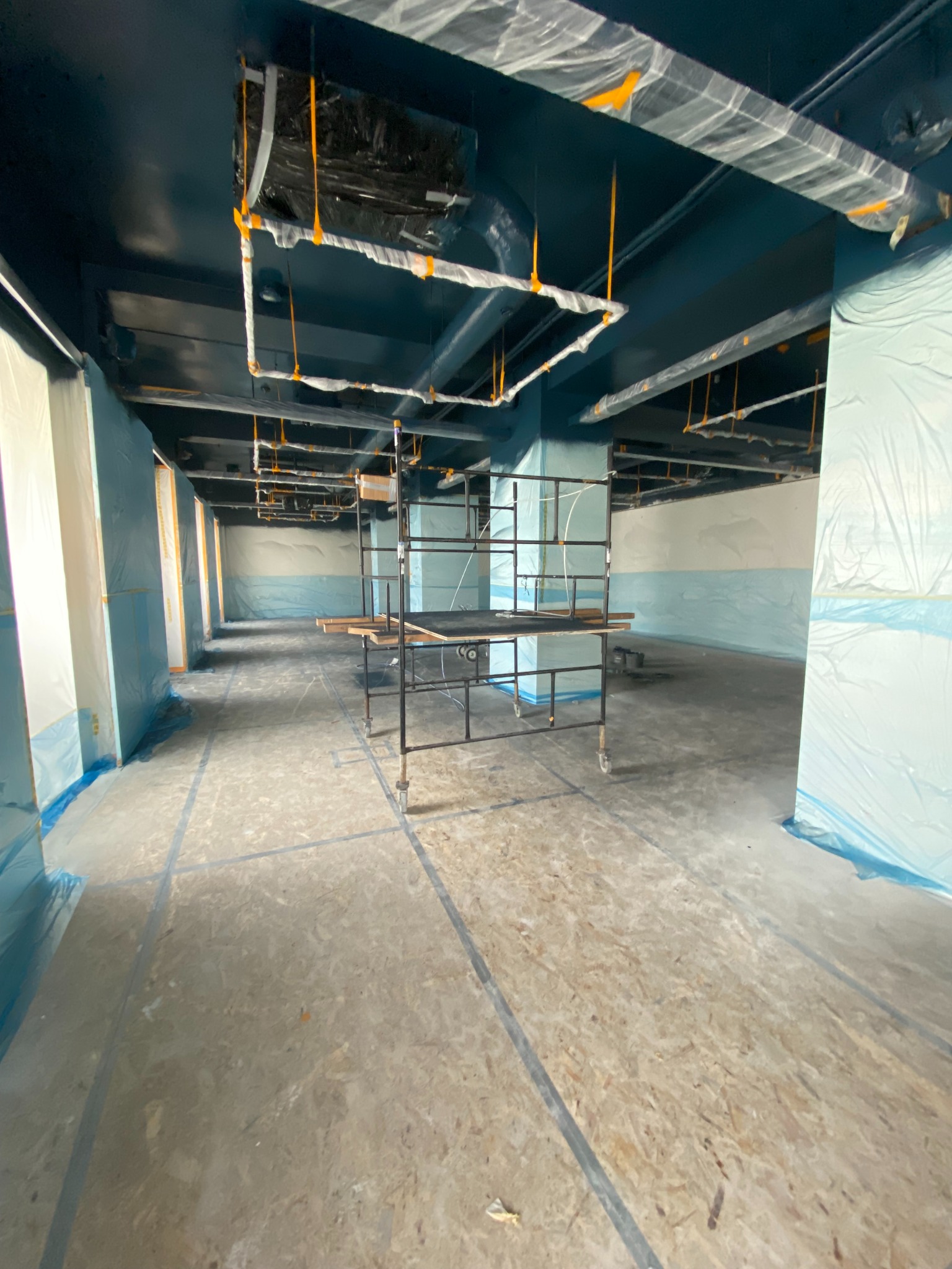 Przygotowane do malowania wnętrze biura: zabezpieczone folią ściany, sufit w kolorze granatowym, widoczne rusztowania. Etap prac przed malowaniem.