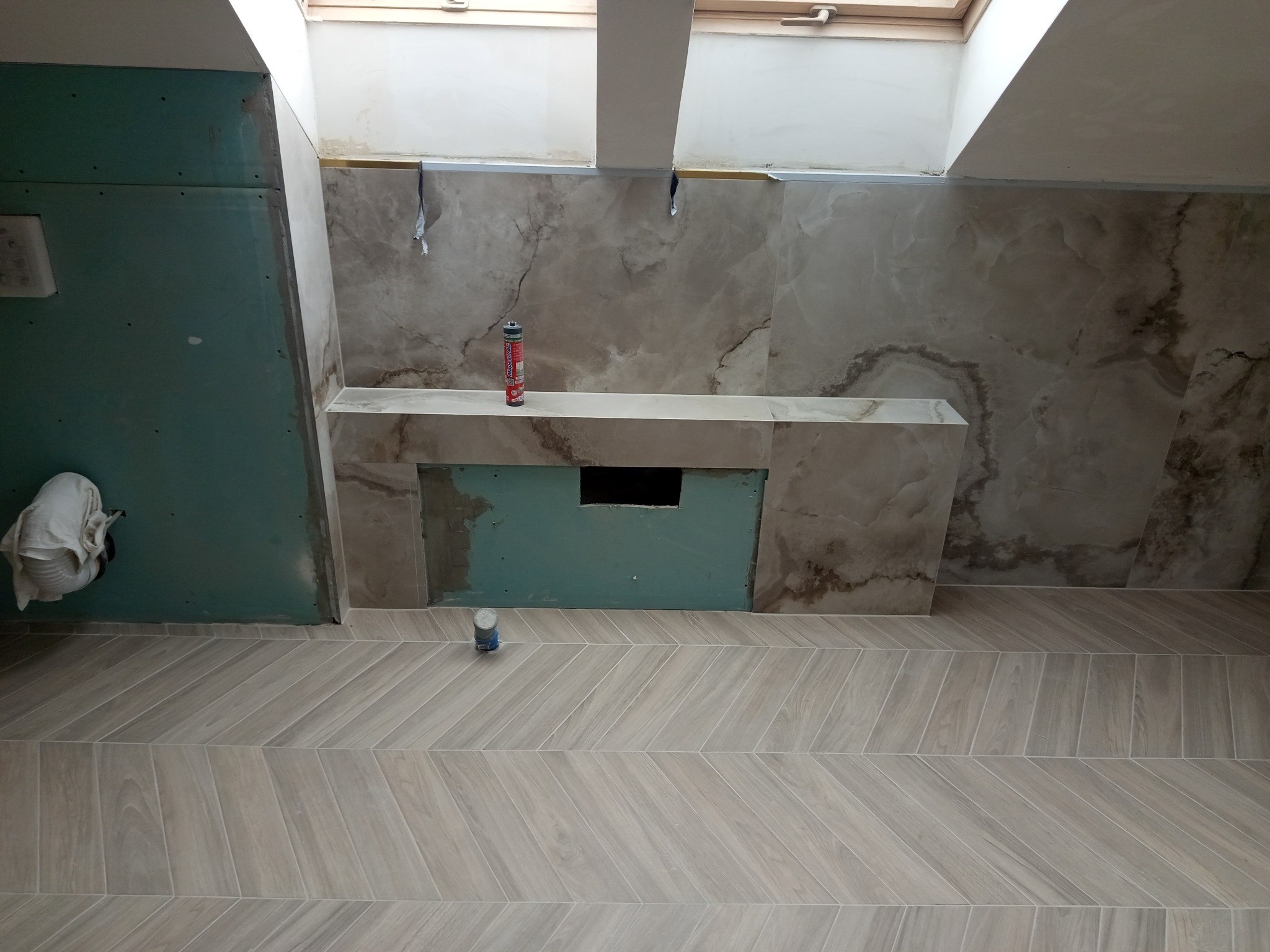 Wnętrze łazienki w trakcie wykończenia: ułożona podłoga z płytek w jodełkę, ściany częściowo wyłożone marmurowymi płytami, widoczne narzędzia i materiały budowlane.