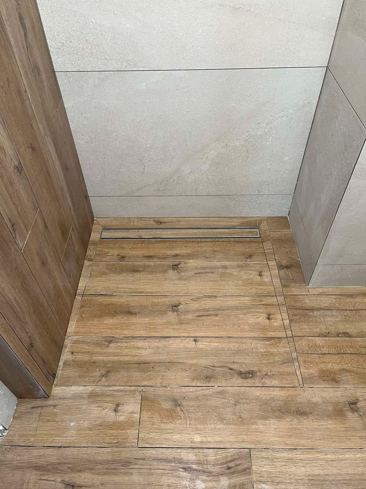 Ukończona podłoga z płytek imitujących drewno w łazience w Niepołomicach, z widocznym odpływem liniowym i szarymi płytkami ściennymi. Detal wykończenia.