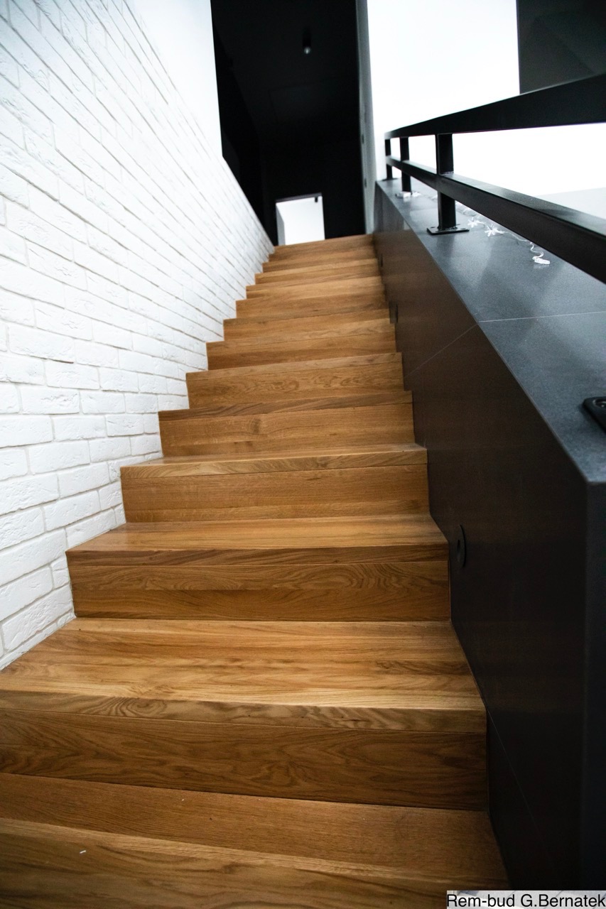 Drewniane schody z dębowymi stopniami, biała ściana z cegły i czarna balustrada. Nowoczesne wykończenie wnętrza z perspektywy dolnej.