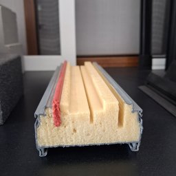 Justyna Pędziwiatr P&Home&Cars - Przekrój profilu okiennego z uszczelką, ukazujący wewnętrzną strukturę i izolację. Widoczne elementy metalowe i piankowe. Prezentacja detali technicznych.