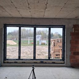 P&Home - Czteroskrzydłowe okno w surowym wnętrzu z widokiem na plac zabaw. Laser krzyżowy na statywie na pierwszym planie. Widoczne ślady po montażu.