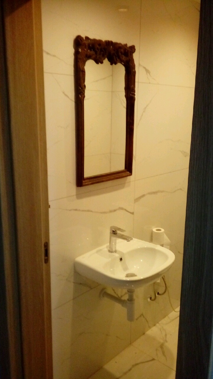 Umywalka narożna z ozdobnym lustrem w wykończonej łazience w Krosno. Białe płytki imitujące marmur. Widok zza otwartych drzwi.