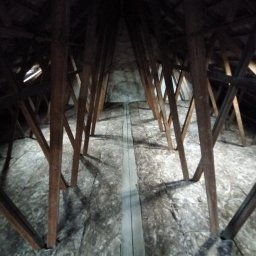 URB usługi remontowo-budowlane - Izolacja poddasza wełną mineralną, widoczne drewniane elementy konstrukcyjne dachu. Ujęcie z perspektywy podłogi, ciemne oświetlenie.