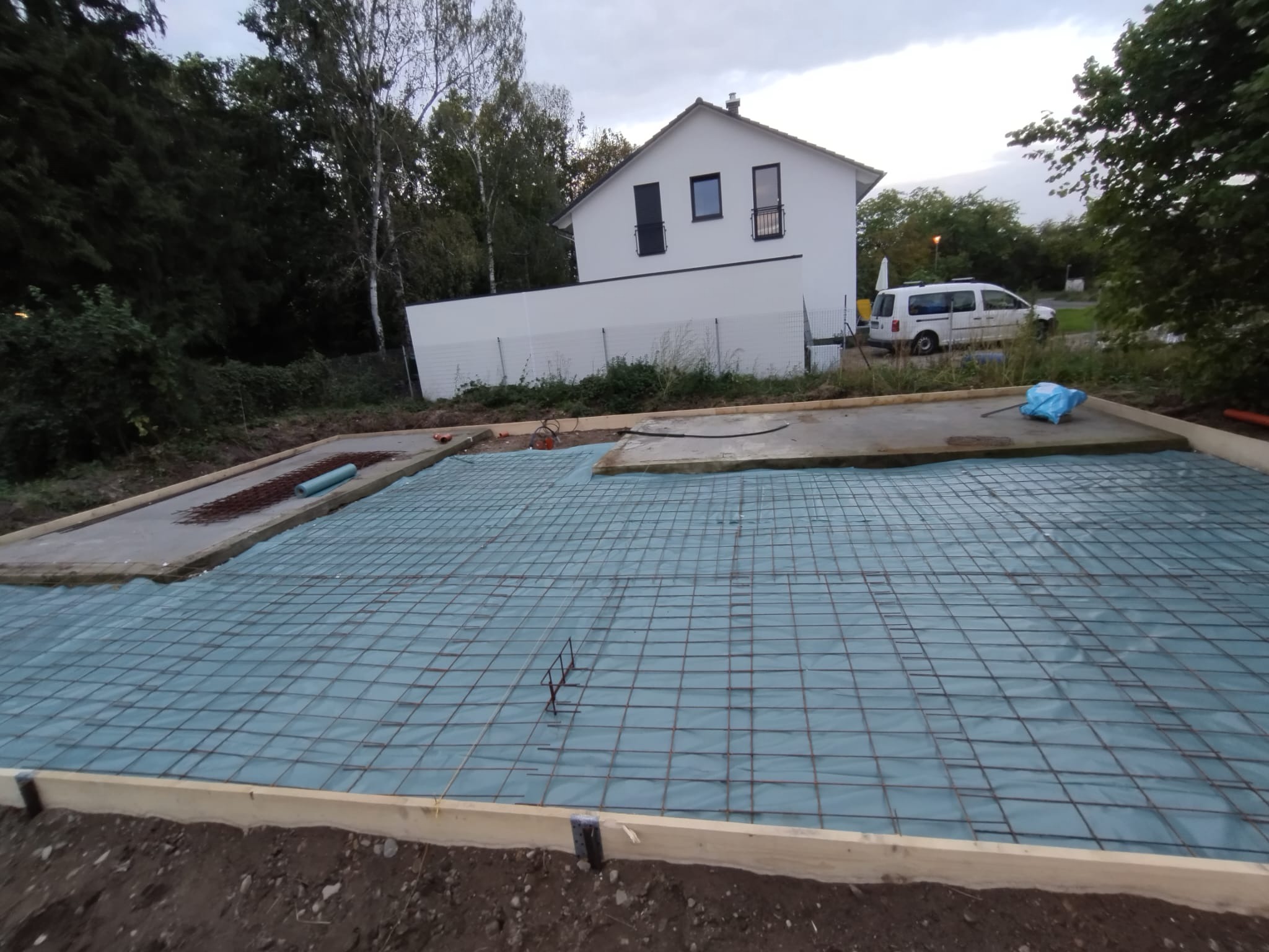 Przygotowanie zbrojenia pod fundamenty domu jednorodzinnego, widok na siatkę zbrojeniową na folii, szalunek drewniany i częściowo wylany beton.