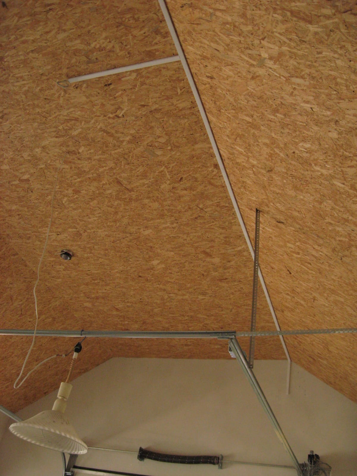 Skośny sufit z płyty OSB w garażu, widoczne elementy konstrukcyjne i oświetlenie, perspektywa od dołu.