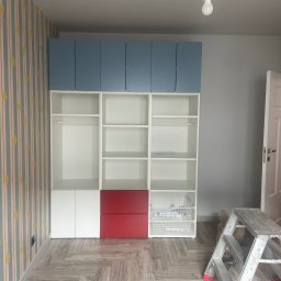 WOJCIECH BIERNACKI - Pokój po remoncie: biało-niebieska szafa z czerwonymi akcentami na tle wzorzystej tapety i szarej ściany. Widoczna drabina malarska.
