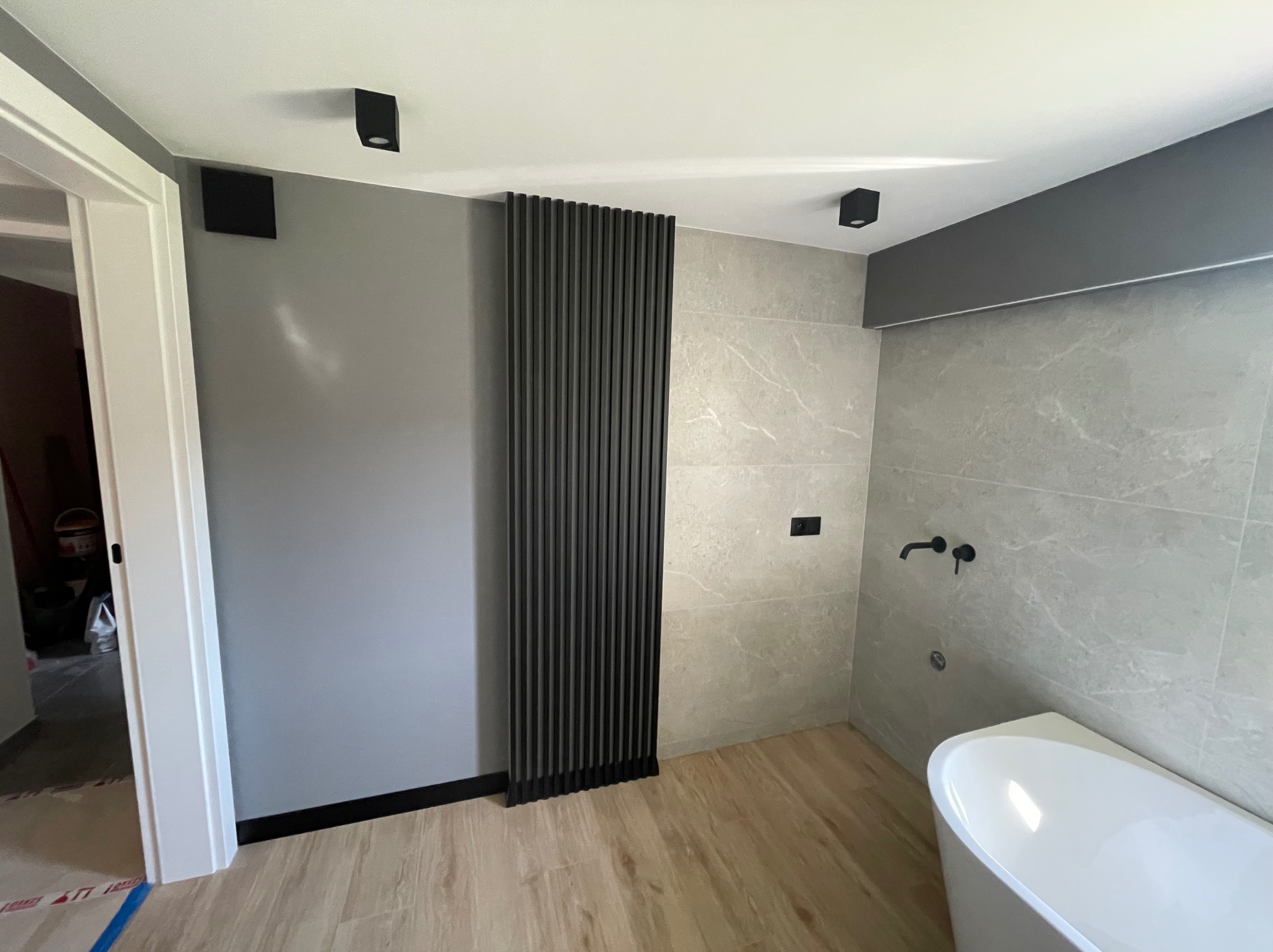 Nowoczesna łazienka po remoncie: szare ściany, drewnopodobne panele, czarna dekoracyjna ścianka z listew, minimalistyczna armatura i oświetlenie.