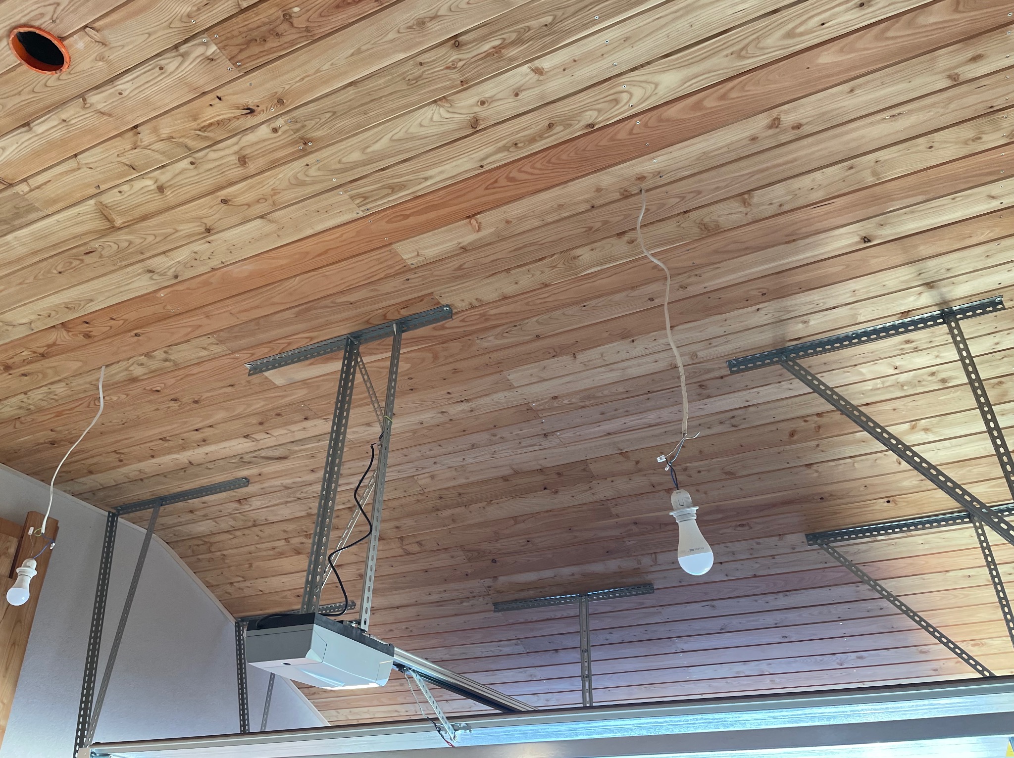 Drewniany sufit z widocznymi belkami i instalacją oświetleniową. Widoczny mechanizm bramy garażowej. Ukośny kadr.