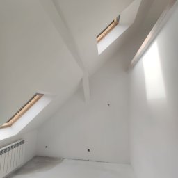 ŁK Wykończenia Wnętrz Łukasz Kłosowski - Białe, świeżo pomalowane poddasze ze skosami i oknami dachowymi. Grzejnik przy ścianie, ślady po szpachlowaniu na podłodze. Minimalistyczne wykończenie.