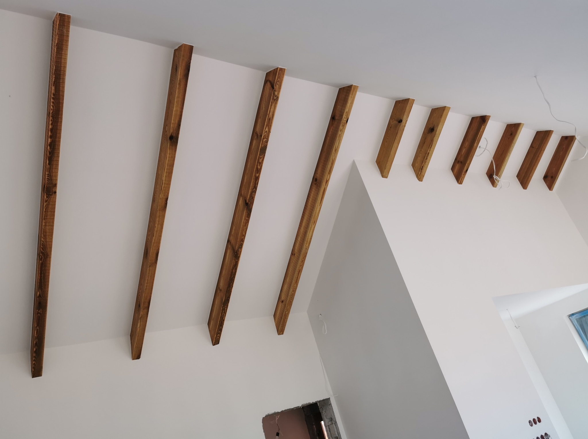 Dekoracyjne, drewniane belki zamontowane na białym suficie, tworzące unikalny element wystroju wnętrza. Widoczne niedokończone prace w tle.