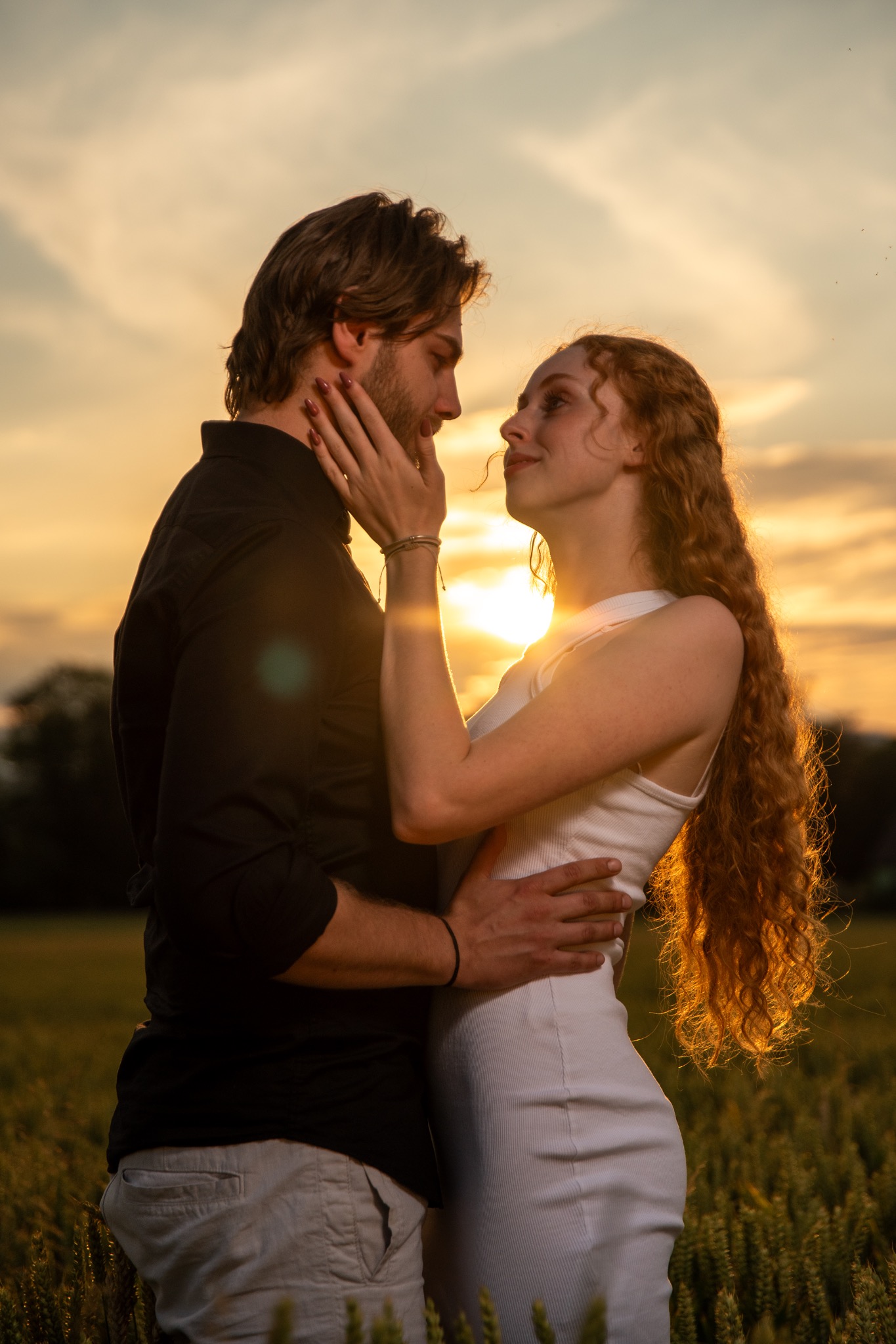 Zakochana para w objęciach na tle zachodzącego słońca. Kobieta z rudymi włosami dotyka twarzy mężczyzny. Romantyczna atmosfera w plenerze.