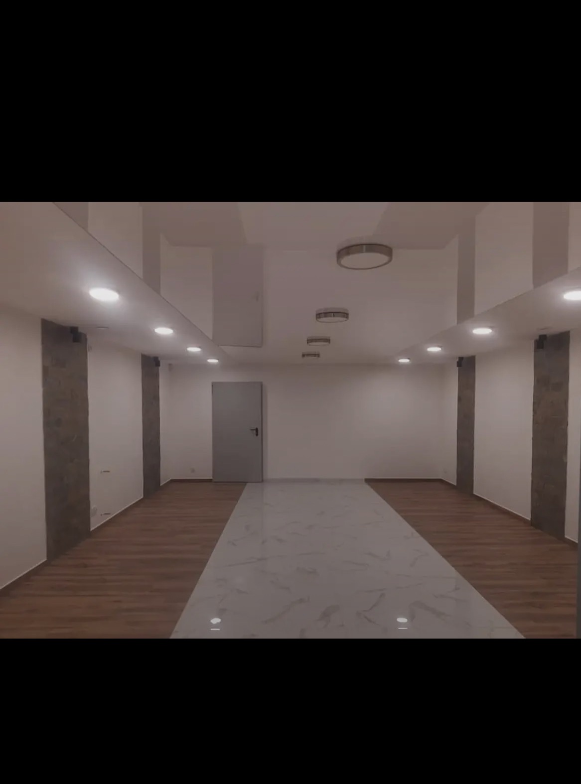 Wykończone wnętrze: parkiet, marmuropodobna posadzka, białe ściany z dekoracyjnymi panelami, sufit z oświetleniem punktowym i centralnym. Szara, zamknięta  drzwi.