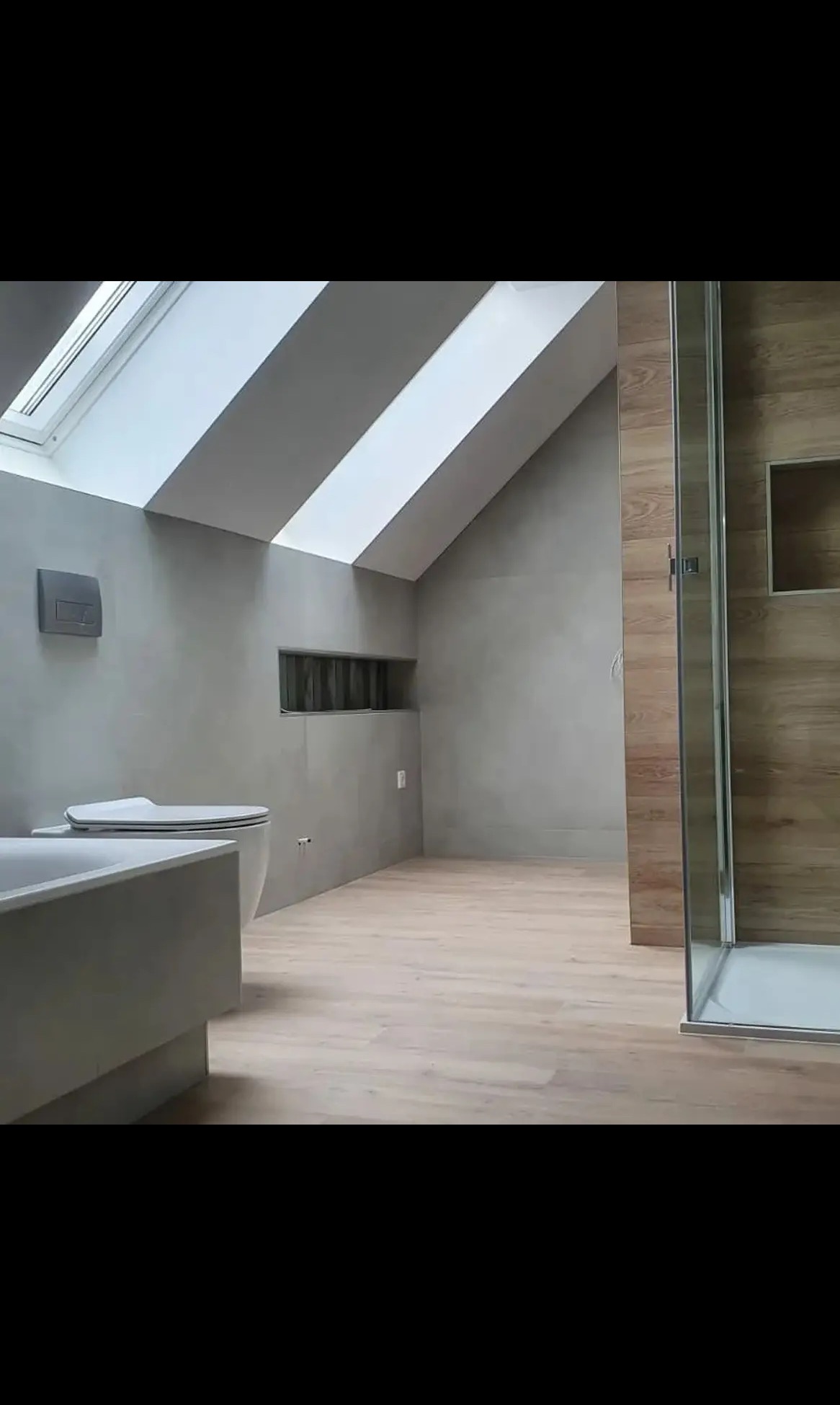 Nowoczesna łazienka na poddaszu z oknem dachowym, szarą armaturą i kabiną prysznicową z drewnopodobnymi panelami. Minimalistyczny design, jasne drewniane panele podłogowe.