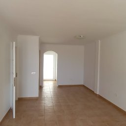 LG Jaworzno - Jasne, przestronne wnętrze po remoncie z terakotą na podłodze. Świeżo pomalowane ściany na biało, widoczne drzwi i przejście do kolejnego pomieszczenia.