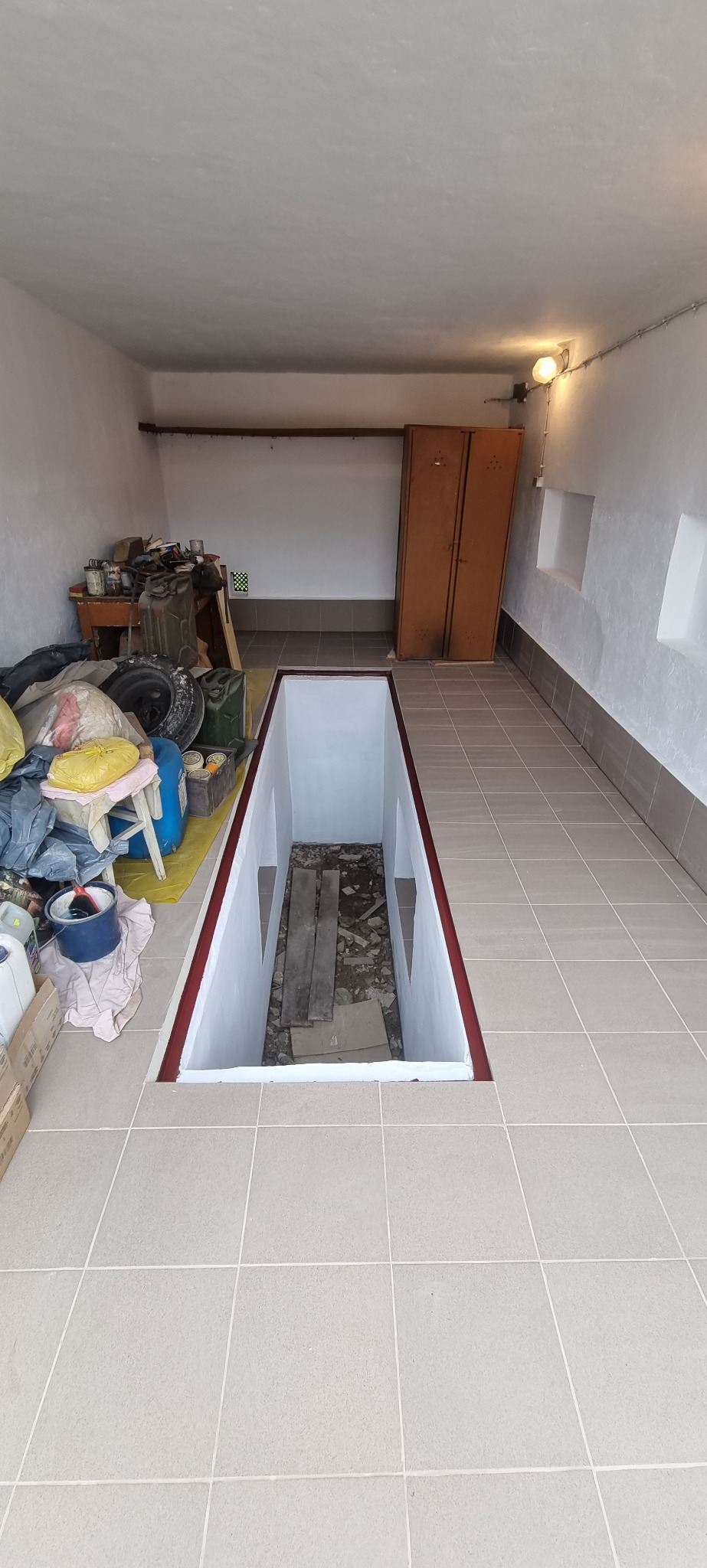 Garaż po remoncie z kanałem samochodowym, wyłożony jasnymi płytkami. Ściany pomalowane na biało, widoczne narzędzia i akcesoria garażowe. Czerwona obwódka kanału.