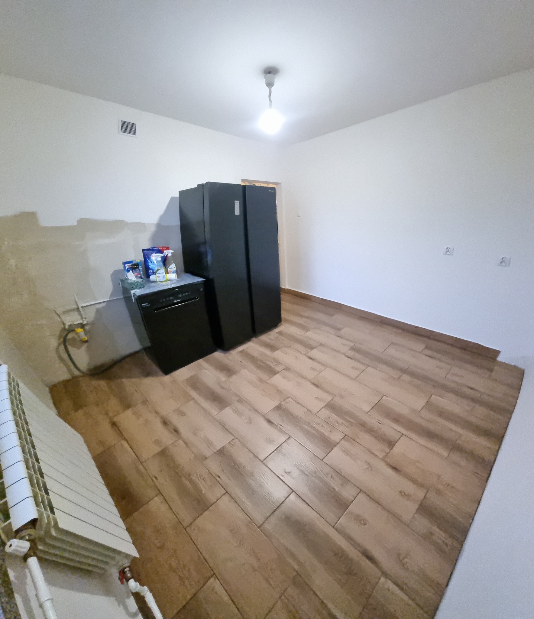 Kuchnia w trakcie remontu: ułożona podłoga z płytek imitujących drewno, ściany częściowo przygotowane do malowania, widoczny grzejnik i sprzęt AGD.