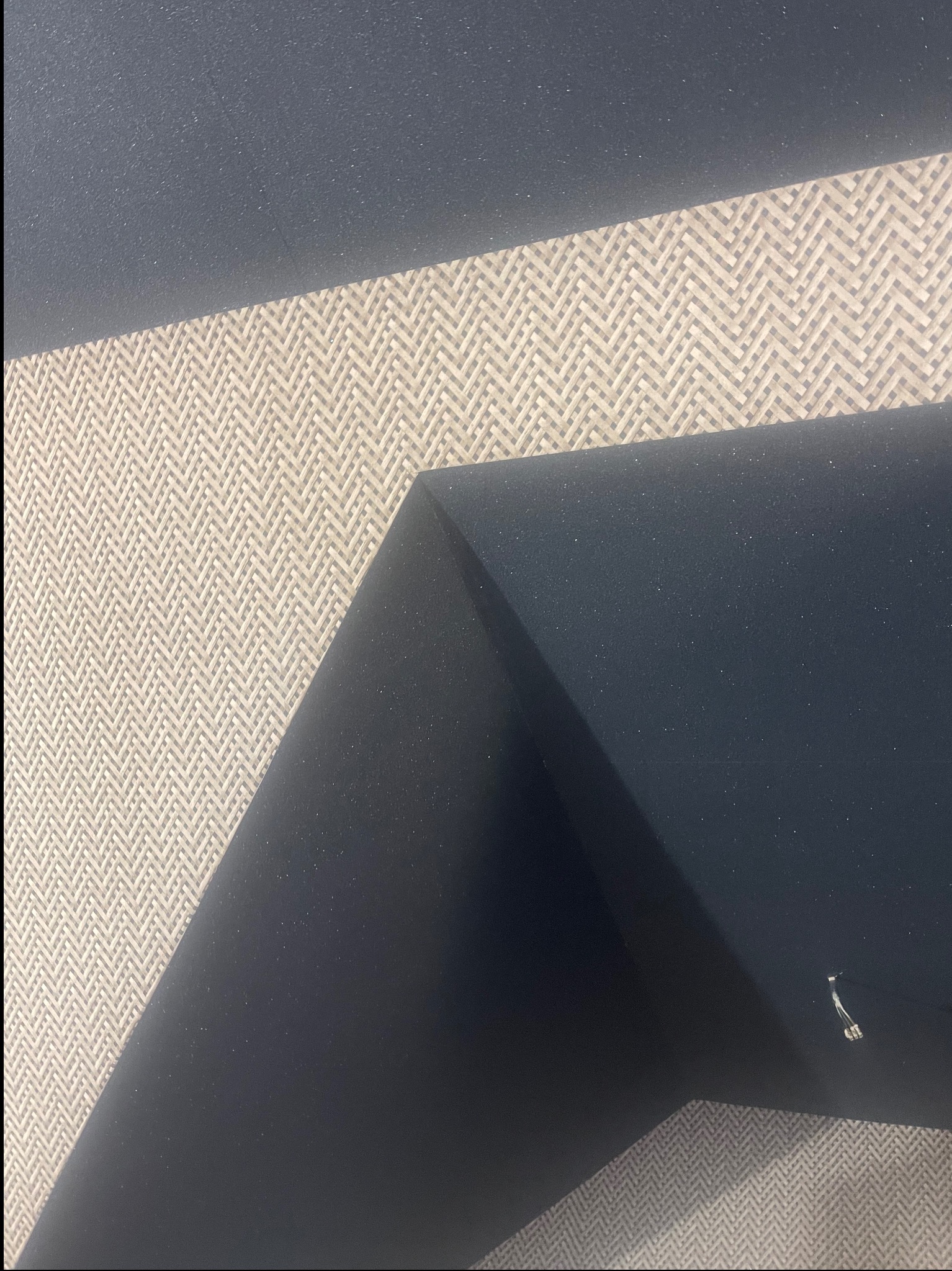 Fragment ściany po wykończeniu: ciemna, gładka powierzchnia styka się z jasną tapetą o wzorze jodełki. Widoczne detale wykończenia i faktura materiałów.