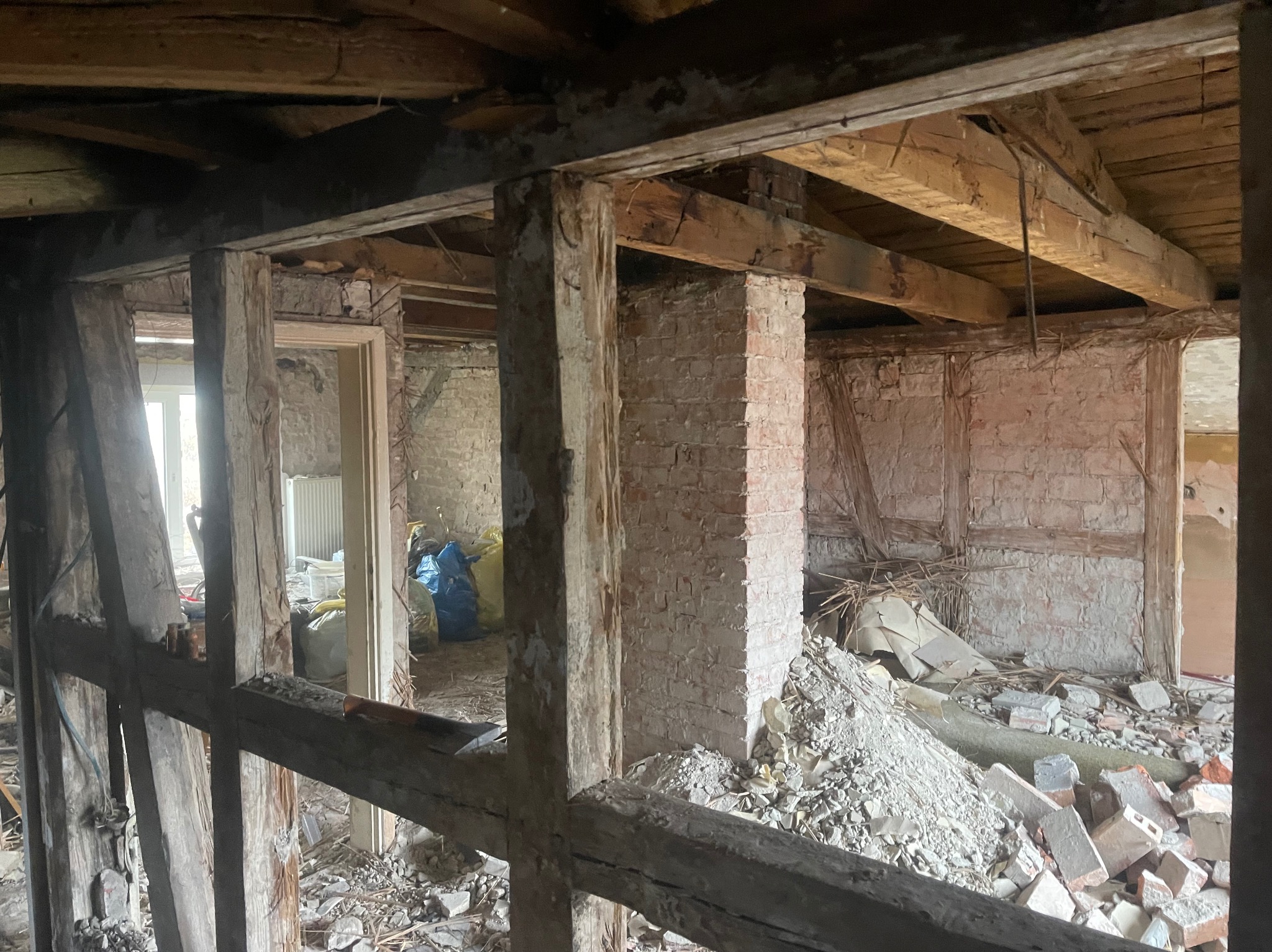Wnętrze w trakcie rozbiórki: odsłonięte cegły, drewniane belki stropowe, gruz. Widoczne worki z odpadami. Ujęcie zza drewnianej konstrukcji szkieletowej.