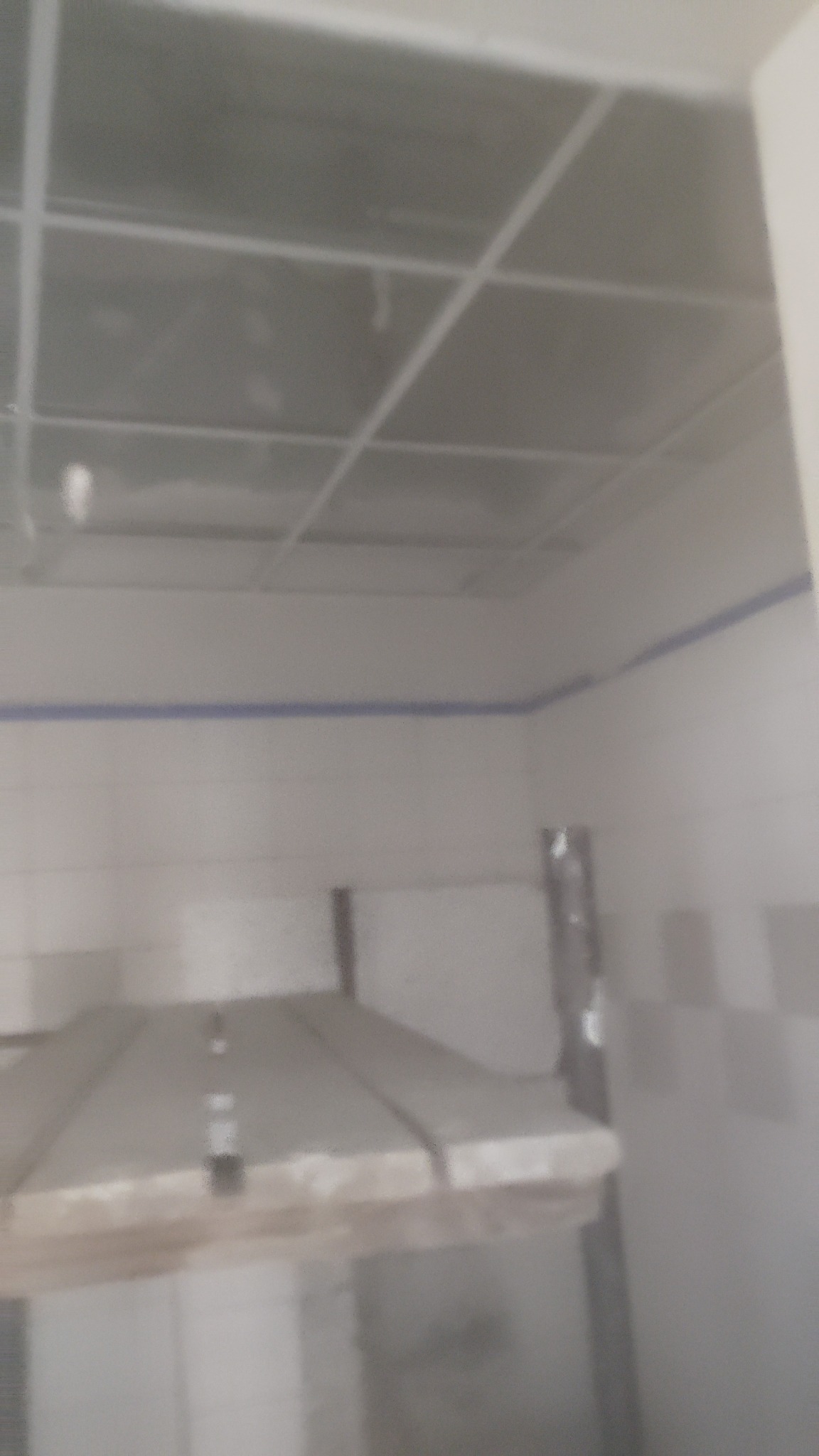 Montaż sufitu podwieszanego z płyt w pomieszczeniu z białymi ścianami i niebieskim akcentem. Widoczna konstrukcja nośna.