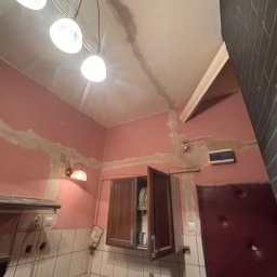 HG-Elektryk SmartTechnika - Różowa kuchnia w trakcie remontu: widoczne ślady po zalaniu na suficie i ścianach, świeżo położona gładź szpachlowa. Ujęcie z dołu, oświetlenie lampą sufitową.
