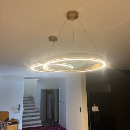 HG-Elektryk SmartTechnika - Nowoczesne, okrągłe lampy LED w Gnieźnie, zawieszone w jasnym wnętrzu w trakcie wykańczania. Widoczne schody i czarna lodówka.