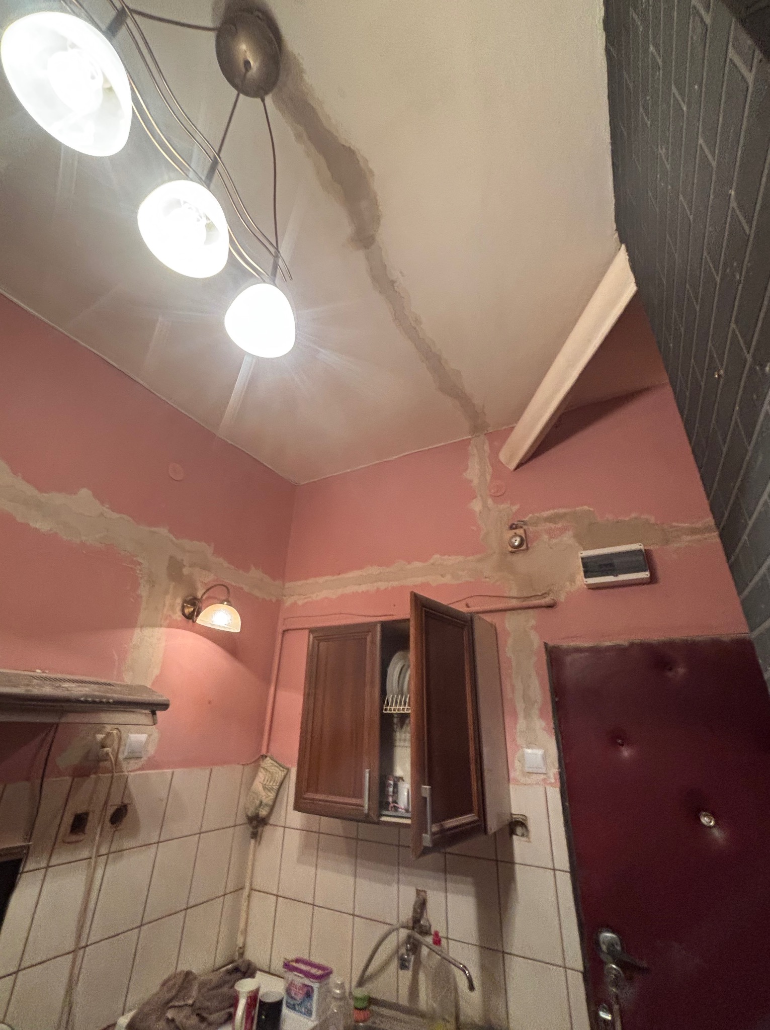 Różowa kuchnia w trakcie remontu: widoczne ślady po zalaniu na suficie i ścianach, świeżo położona gładź szpachlowa. Ujęcie z dołu, oświetlenie lampą sufitową.