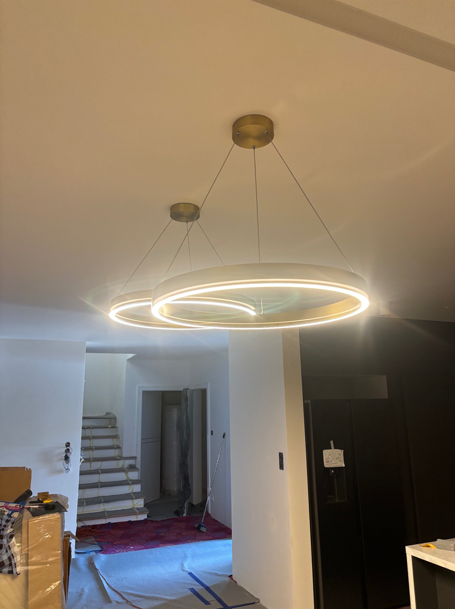 Nowoczesne, okrągłe lampy LED w Gnieźnie, zawieszone w jasnym wnętrzu w trakcie wykańczania. Widoczne schody i czarna lodówka.