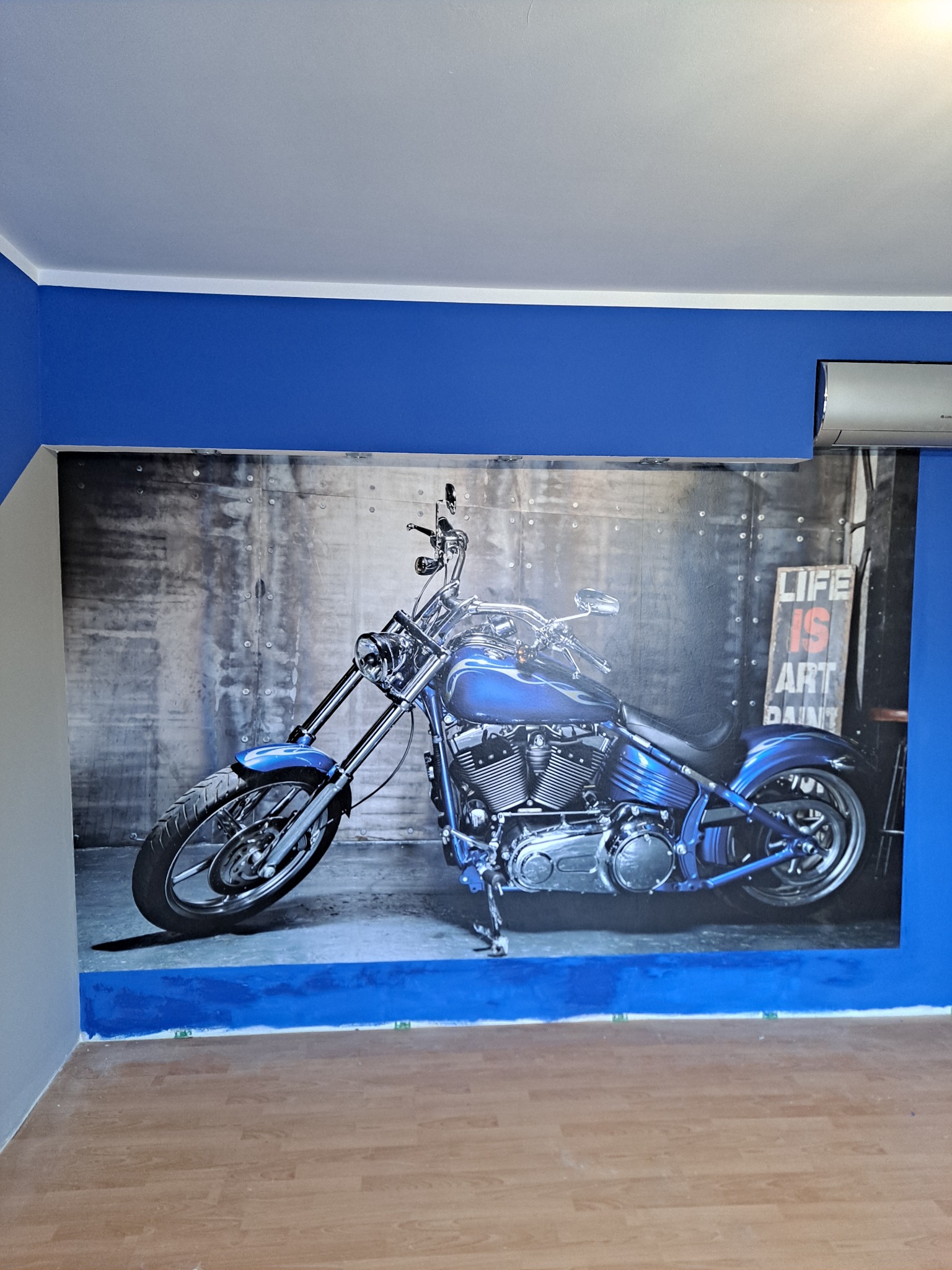 Fototapeta z motywem motocykla w niebieskim pokoju z drewnianą podłogą. Na ścianie widoczny klimatyzator.