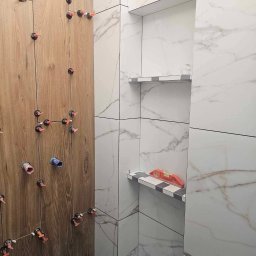 Wykończenia - Ściana łazienki w trakcie wykańczania: imitacja drewna i marmurowe płytki, system poziomowania płytek, półki wnękowe z poziomnicą. Detal układania płytek.