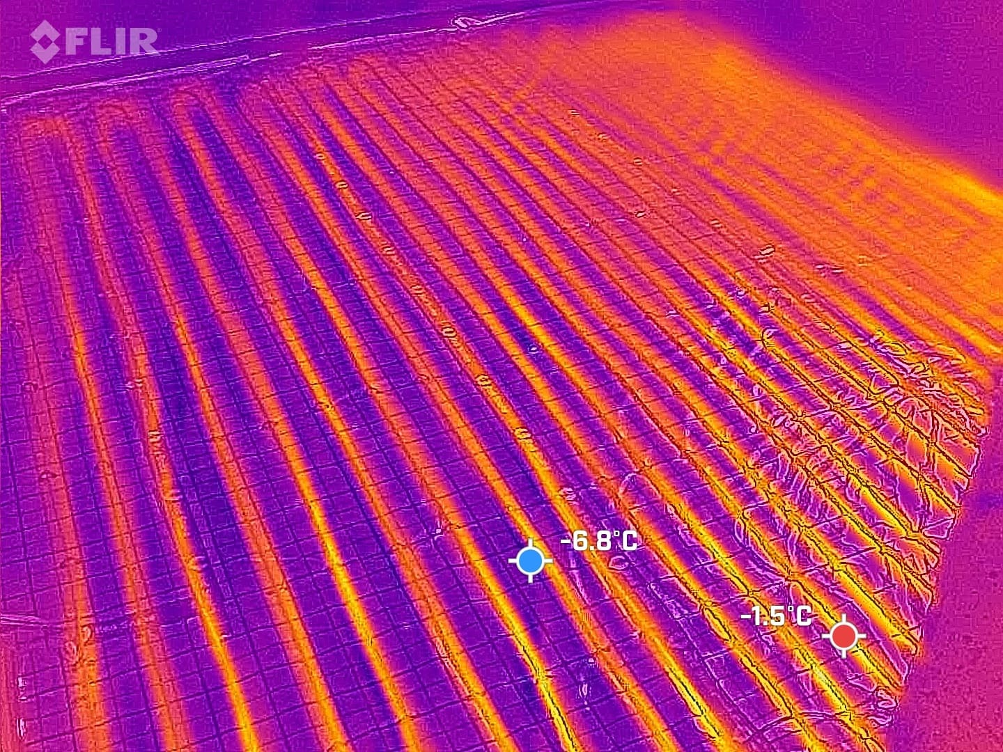Termowizyjne zdjęcie podłogówki w trakcie pracy, ukazujące rozkład temperatur. Widoczne rury grzewcze w odcieniach pomarańczy na fioletowym tle.