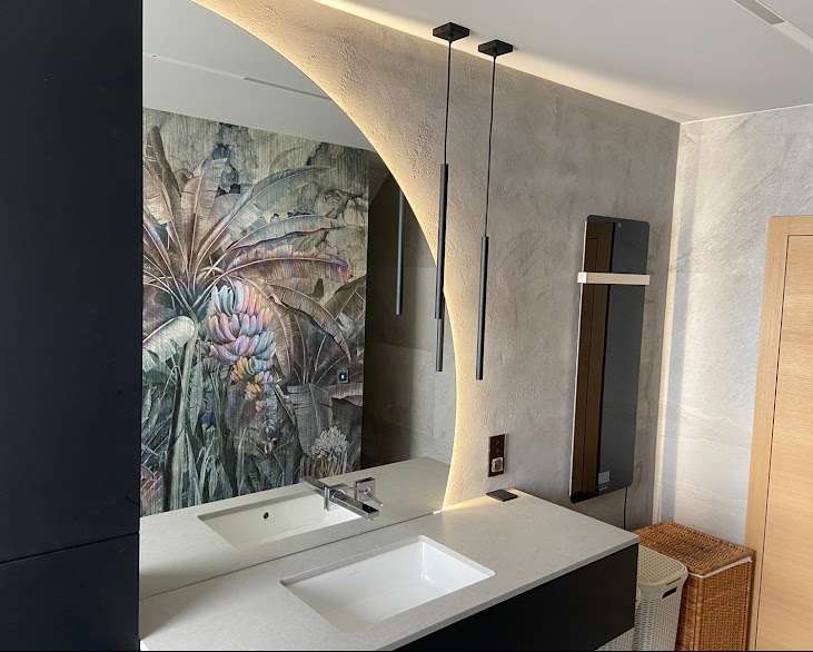 Nowoczesna łazienka z podwójną umywalką, lustrem z podświetleniem LED i tapetą w tropikalne wzory. Minimalistyczne lampy wiszące i grzejnik drabinkowy.