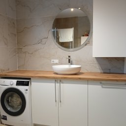 Stolarnia Gwiaździsta Grzegorz Kazanowski - Nowoczesna łazienka z drewnianym blatem, okrągłym lustrem i białą umywalką nablatową. Pralka Electrolux wkomponowana w zabudowę. Marmurowe płytki na ścianie.