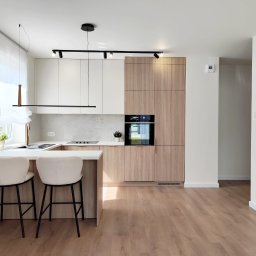 Stolarnia Gwiaździsta Grzegorz Kazanowski - Jasna kuchnia z drewnianymi i białymi szafkami, oświetleniem punktowym i dwoma krzesłami barowymi. Minimalistyczny design, naturalne światło.