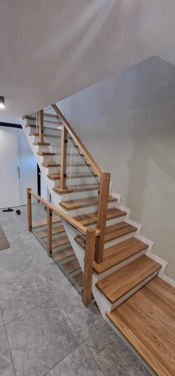 Nowoczesne schody drewniane z jasnymi stopniami i szklaną balustradą, widok z dołu, szare płytki podłogowe, minimalistyczny design.