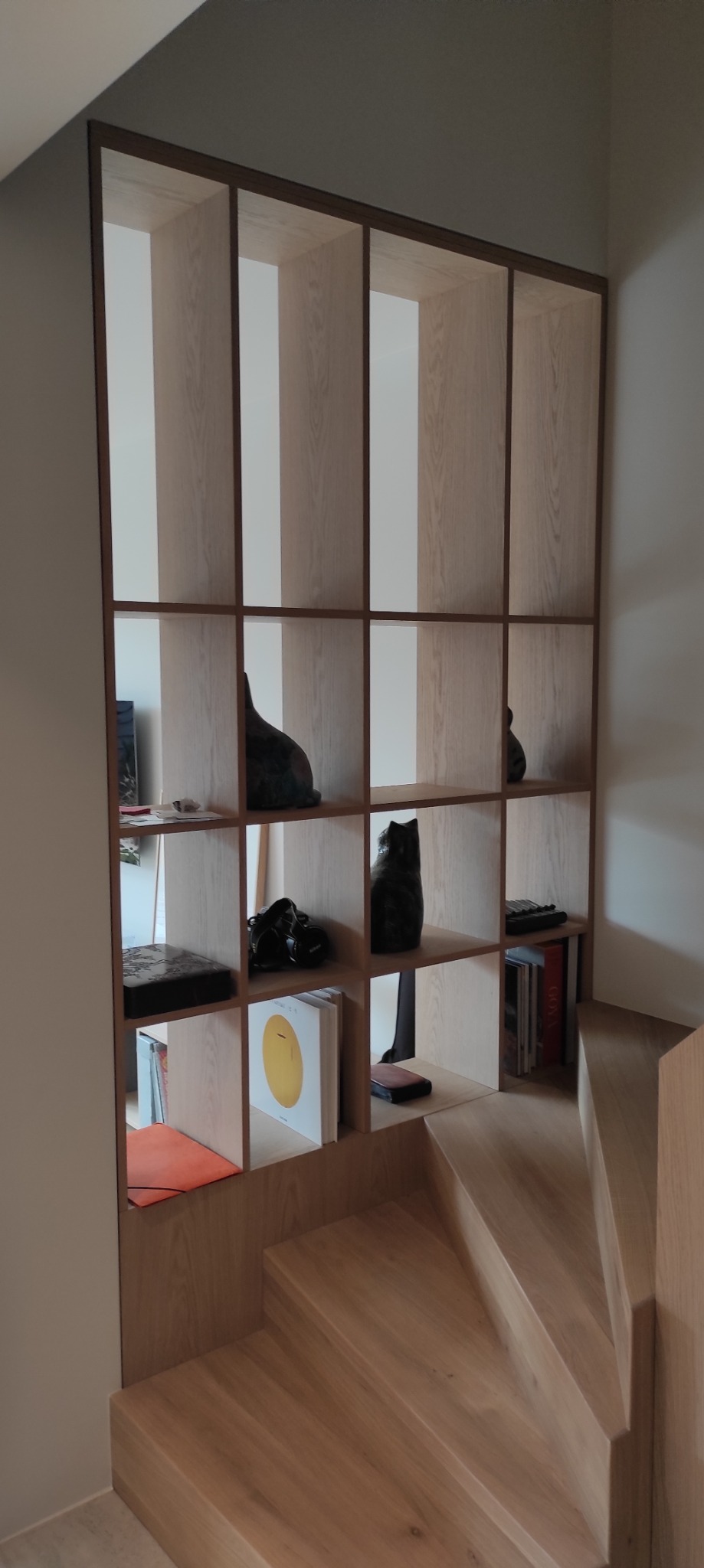 Drewniany regał schodkowy z dekoracjami, wykonany na wymiar, zintegrowany ze schodami. Jasne drewno, minimalistyczny design, nowoczesne wnętrze.