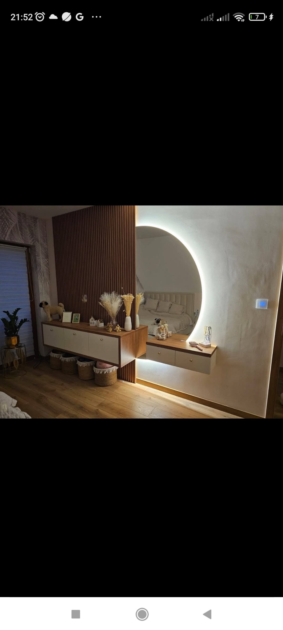 Nowoczesna aranżacja wnętrza z drewnianą ścianką działową, szafką z koszami i okrągłym lustrem z podświetleniem LED, odbijającym łóżko. Ciepłe oświetlenie i drewniana podłoga.