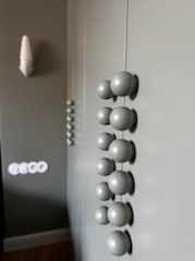 Szara szafa wnękowa z nietypowymi, kulistymi uchwytami, widoczna z boku, z elementami dekoracyjnymi na ścianie w tle. Ujęcie z perspektywy, lekko rozmyte.