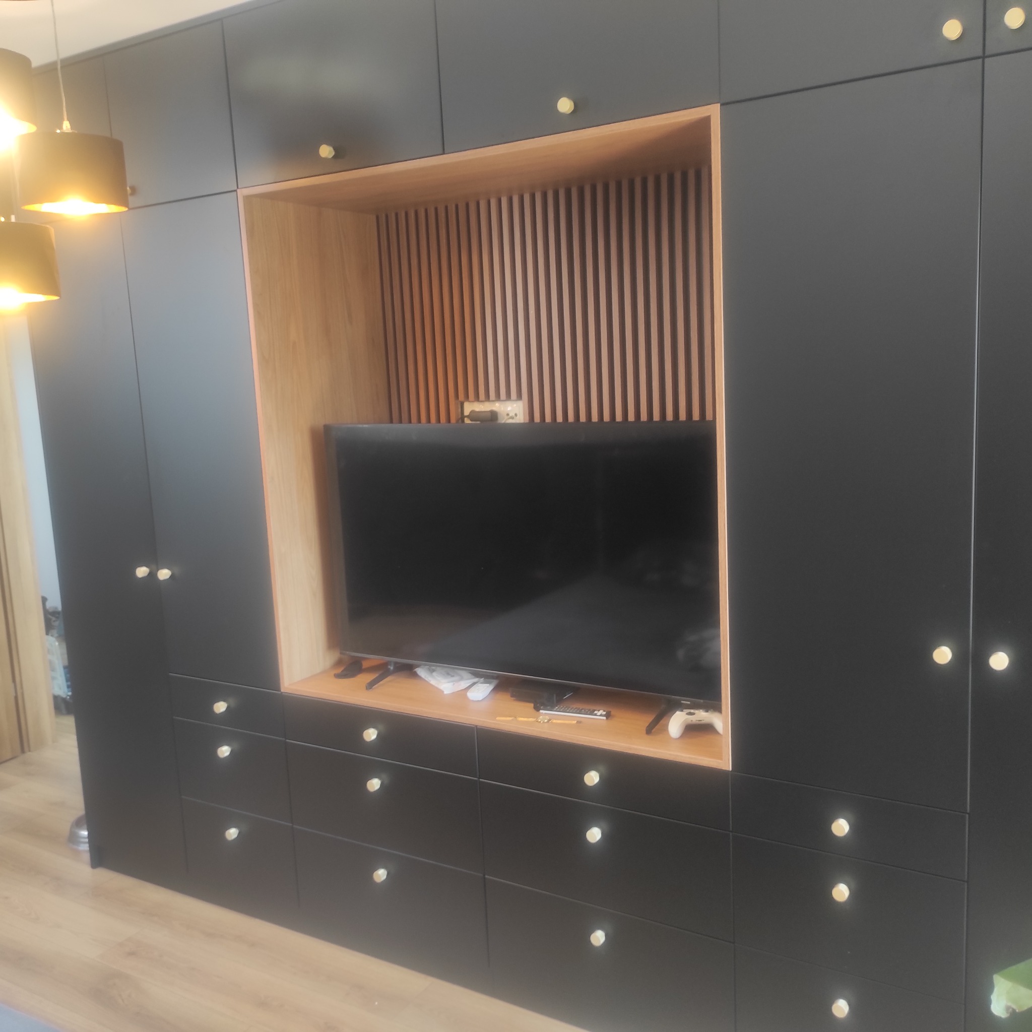 Czarna szafa wnękowa z drewnianą wnęką na telewizor i złotymi gałkami, wykonana na wymiar w Warszawie. Nowoczesny design i funkcjonalność.