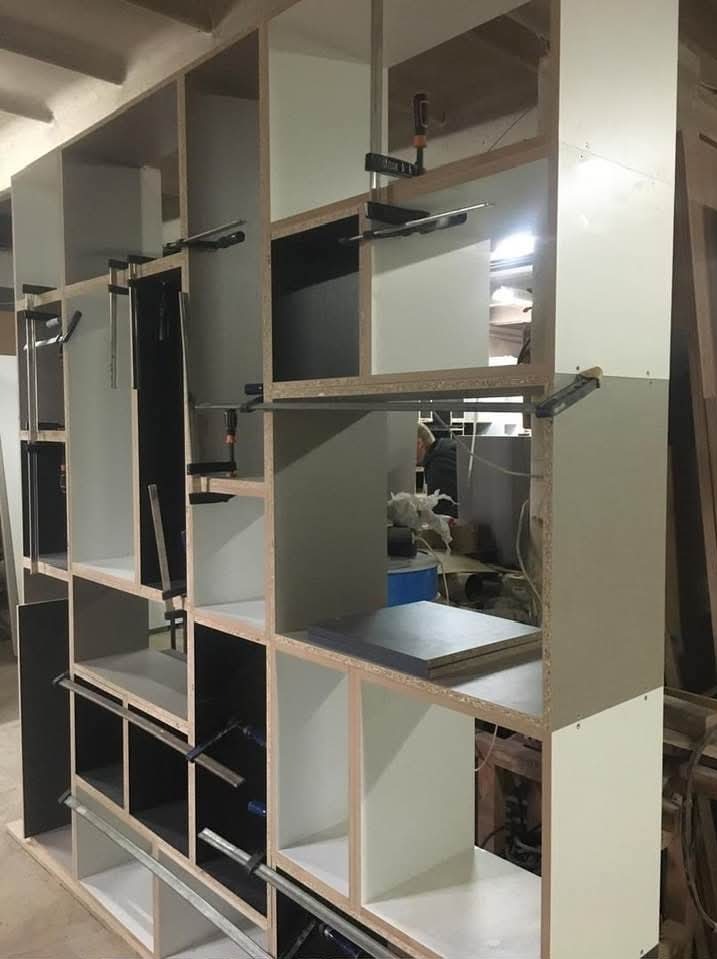 Szafa wnękowa w trakcie montażu: widoczne elementy konstrukcyjne, białe i czarne półki, ściski stolarskie. Ujęcie z bliska, ukazujące detale łączeń.
